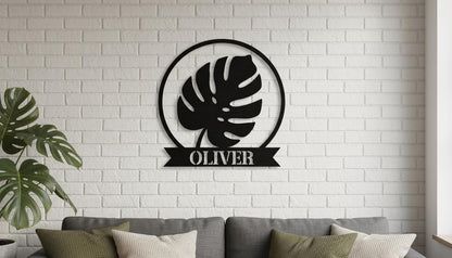 a black metal sign with a leaf design hanging on a white brick wall above a gray couch with pillows.