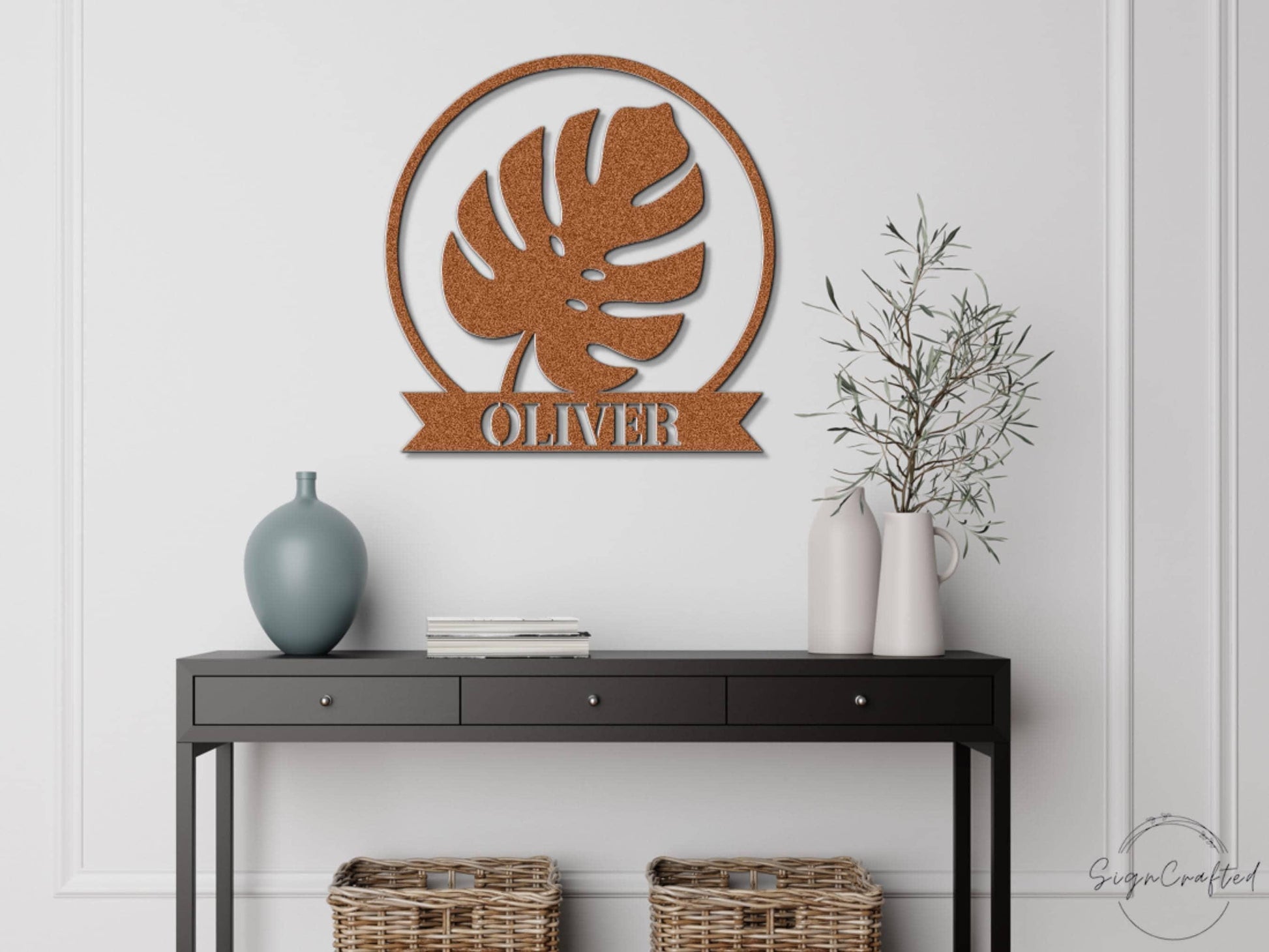 a black console table with a vase, a book, and a plant on it, along with a wall-mounted metal sign that reads "OLIVER".