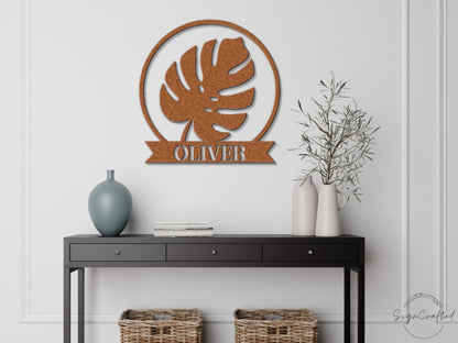 a black console table with a vase, a book, and a plant on it, along with a wall-mounted metal sign that reads "OLIVER".