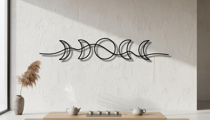 a minimalist design with a wall art piece depicting the phases of the moon, including crescent, waxing, full, and waning. The art piece is mounted on a white wall, and there is a wooden table with a teapot and cups in front of it.