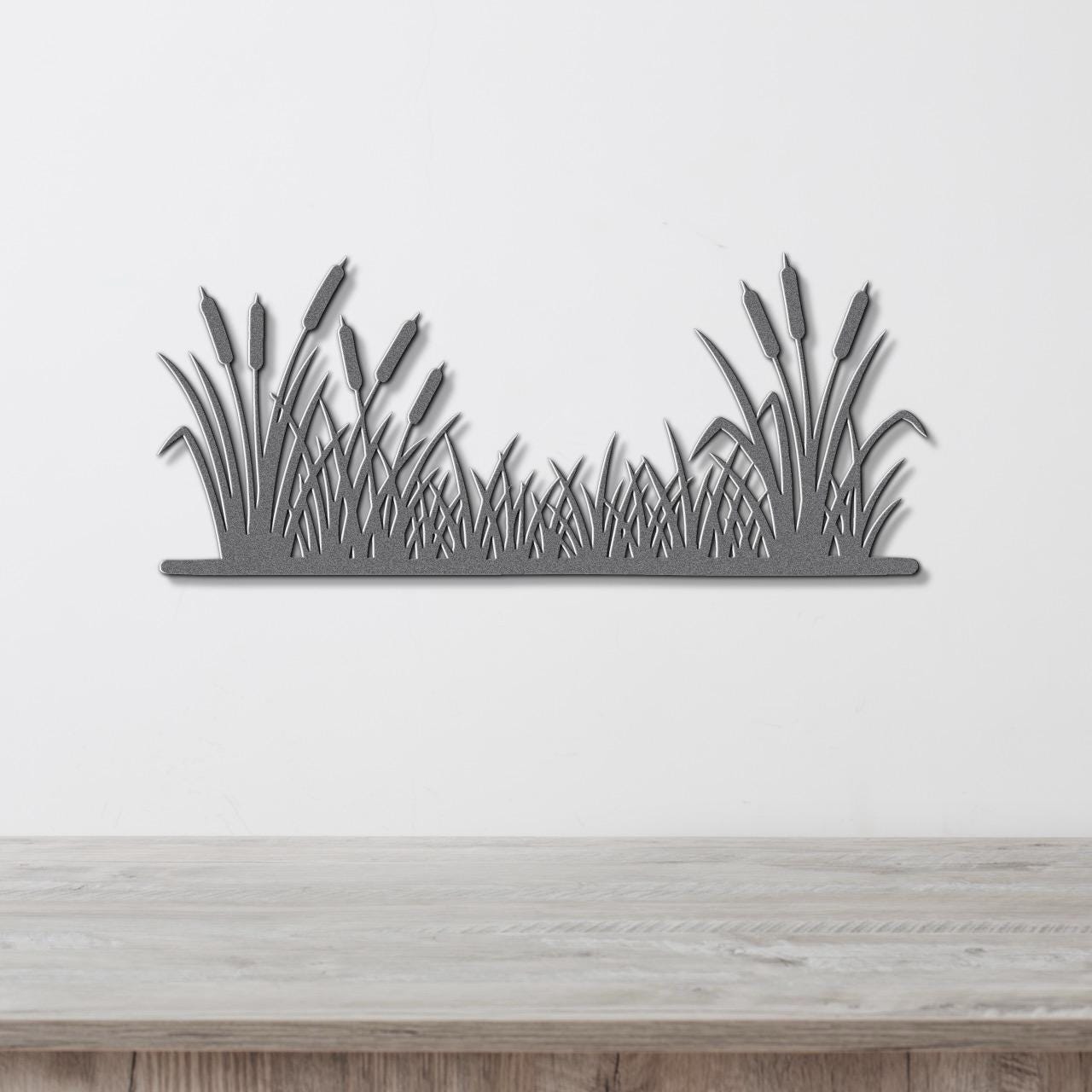 A silhouette of reeds or grasses is displayed on a white wall above a wooden table.