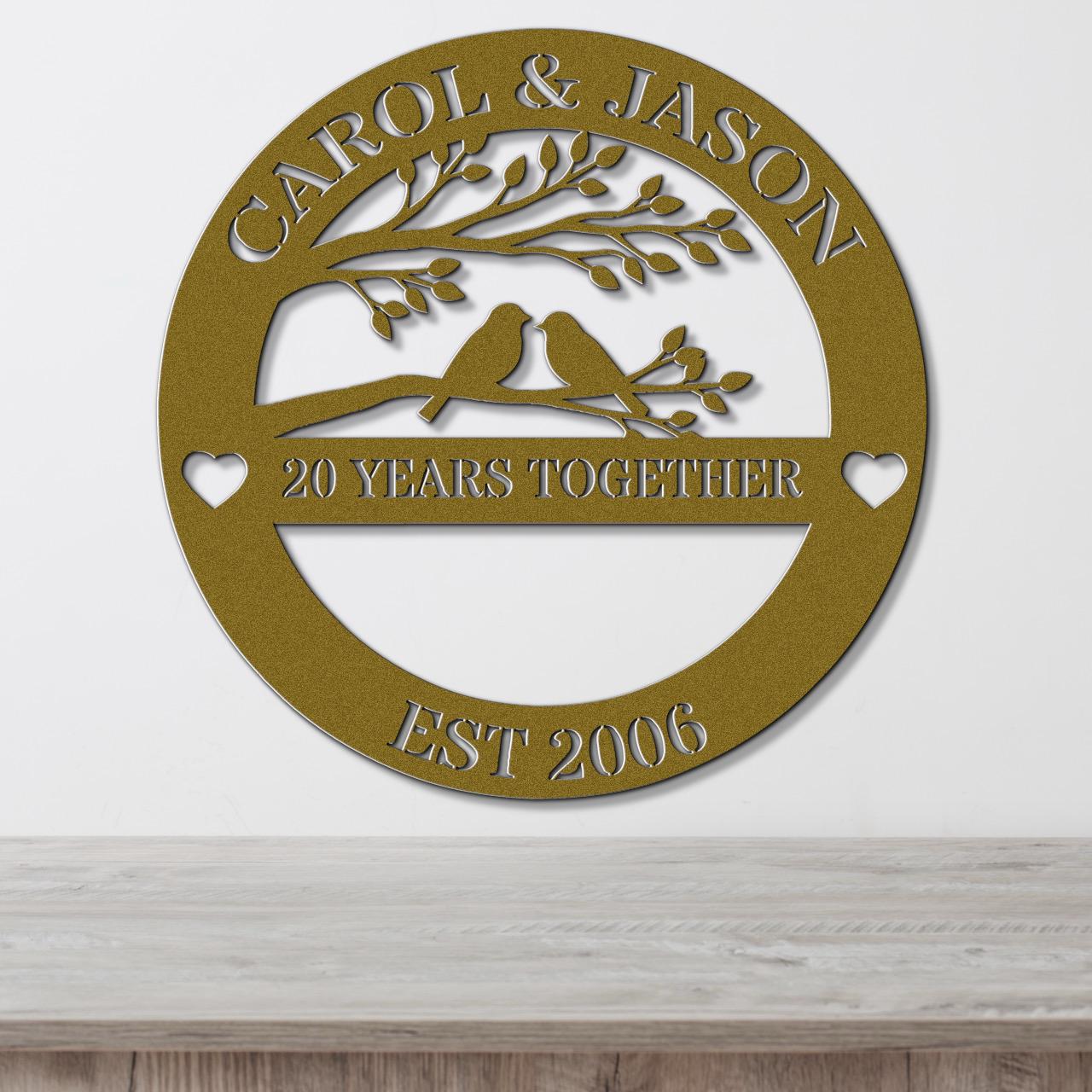 A gold-colored metal sign with the text "CAROL & JASON" and "20 YEARS TOGETHER EST 2006" on it, along with a tree silhouette and two birds.