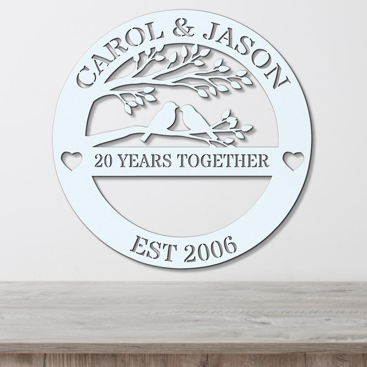 A white circular sign with the text "CAROL & JASON" and "20 YEARS TOGETHER EST 2006" on it, along with a tree silhouette and two birds.