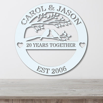 A white circular sign with the text "CAROL & JASON" and "20 YEARS TOGETHER EST 2006" on it, along with a tree silhouette and two birds.