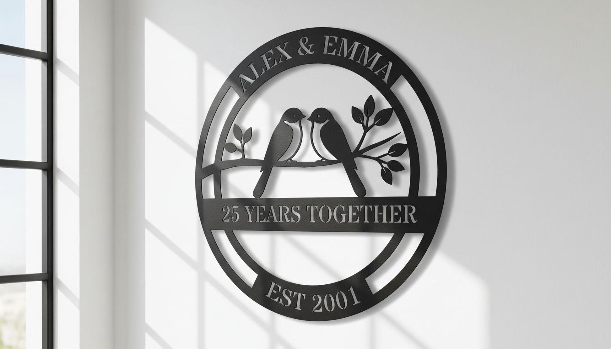 A black metal sign with the text "Alex & Emma" and "25 YEARS TOGETHER EST 2001" on it, along with a graphic of two birds sitting on a branch.
