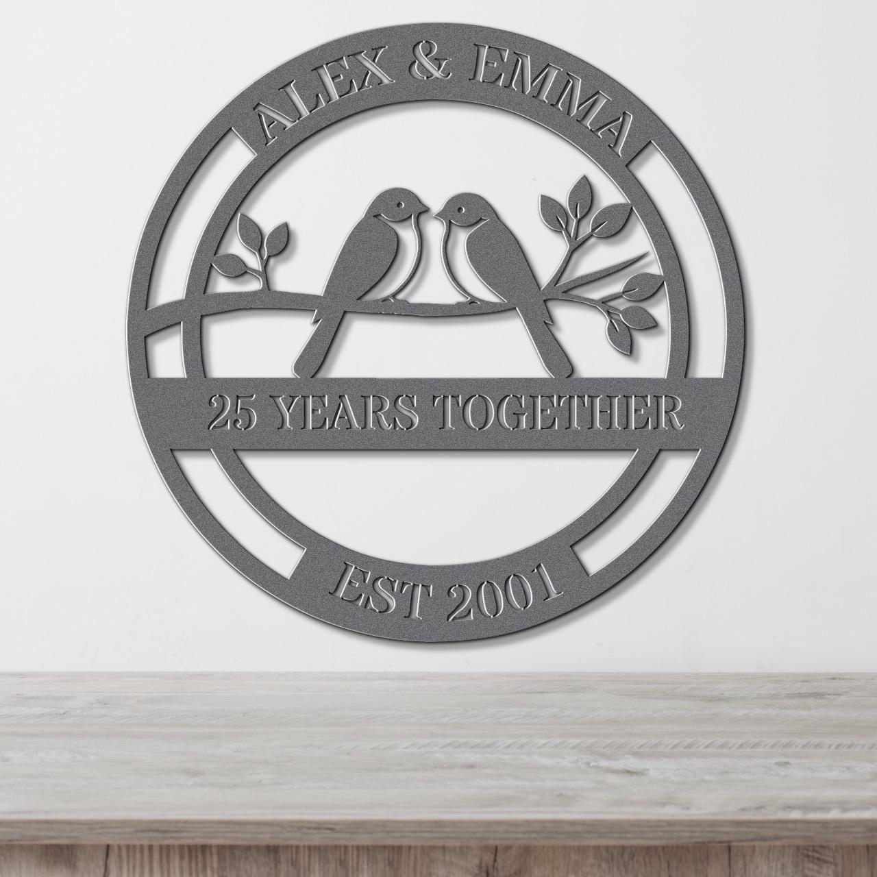 A metal sign with the text "Alex & Emma" and "25 YEARS TOGETHER EST 2001" on it, along with a bird silhouette.