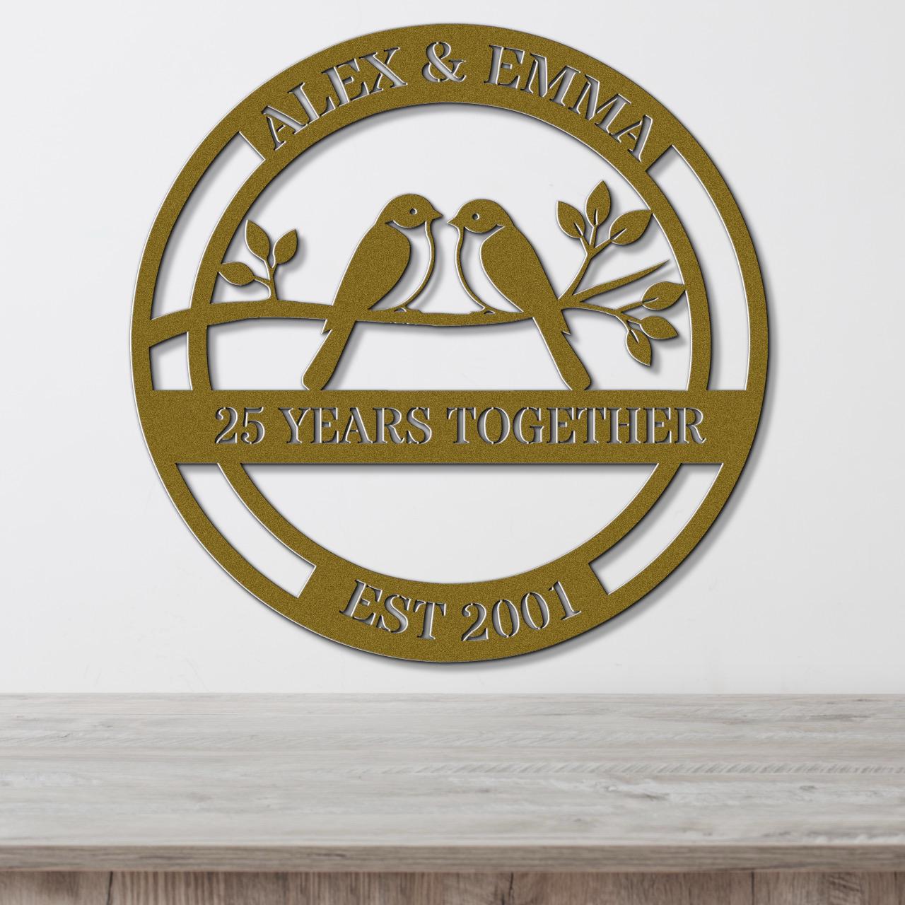 A gold-colored metal sign with the text "Alex & Emma" and "25 YEARS TOGETHER EST 2001" on it, along with a bird silhouette.