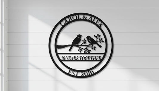 A black and white metal sign with the text "CAROL & ALEX 10 YEARS TOGETHER EST 2016" and a graphic of two birds perched on a branch.