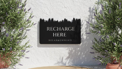 a sign that reads "RECHARGE HERE" with the phrase "RELAX&UNWIND" below it. The sign is mounted on a wall, and there are potted plants on either side of it.