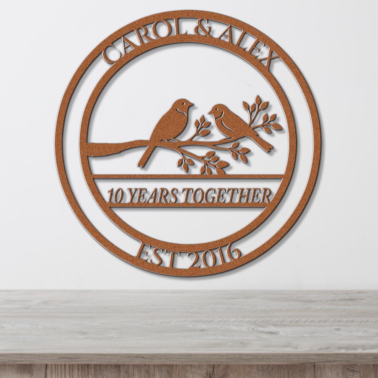 A circular metal sign with the text "CAROL & ALEX 10 YEARS TOGETHER EST 2016" and a bird silhouette on a branch.