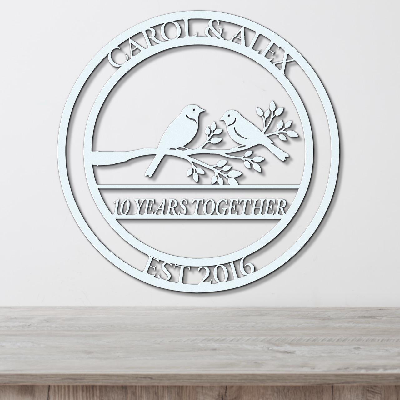 A white circular wall hanging with the text "CAROL & ALEX 10 YEARS TOGETHER EST 2016" and a graphic of two birds perched on a branch.