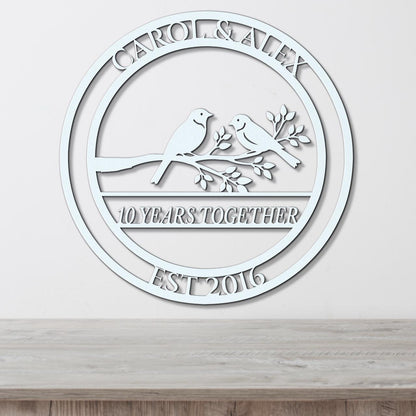 A white circular wall hanging with the text "CAROL & ALEX 10 YEARS TOGETHER EST 2016" and a graphic of two birds perched on a branch.