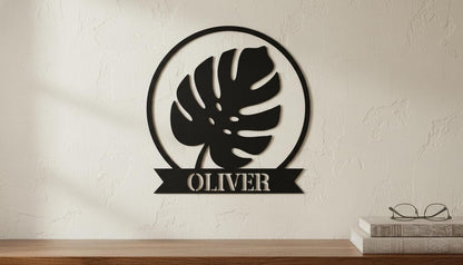 a wall decoration with a large leaf-shaped design and the name "OLIVER" below it, mounted on a wall.