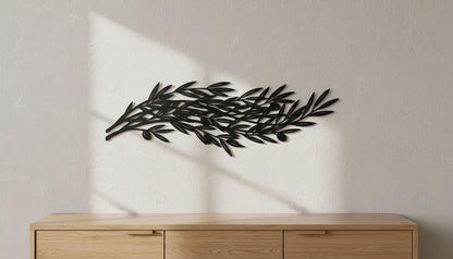 A black metal leaf sculpture is mounted on a white wall above a wooden cabinet or dresser.