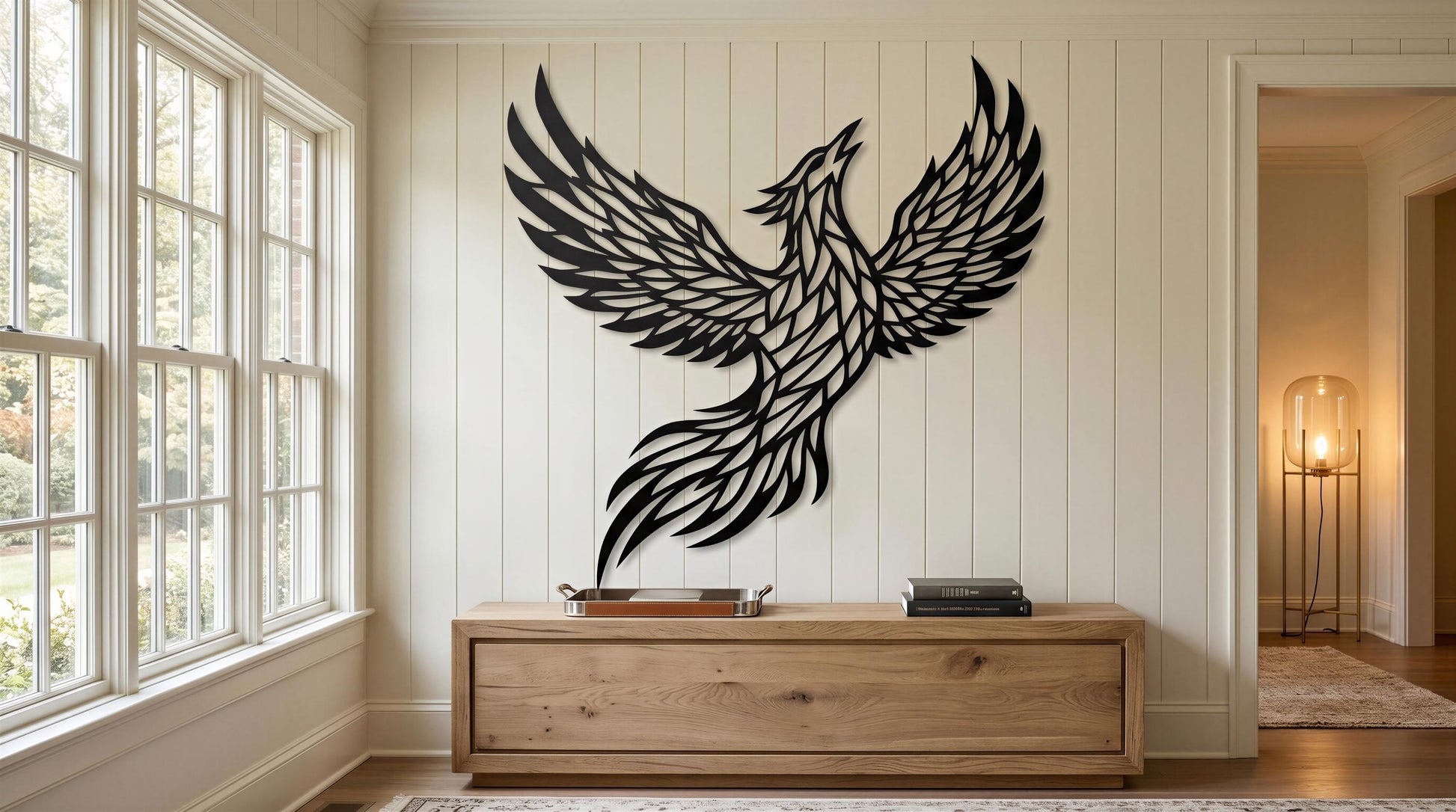 a large black bird sculpture with outstretched wings, mounted on a white wall in a room with a wooden dresser and a window.