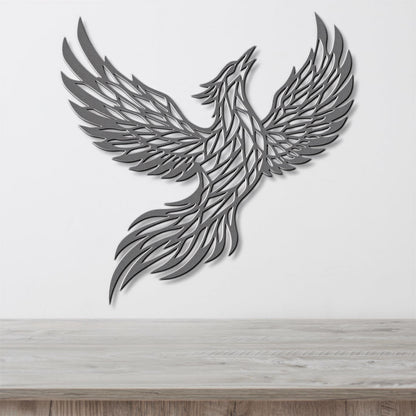 A stylized metal sculpture of a bird in flight, with intricate patterns and designs, mounted on a white wall above a wooden surface.