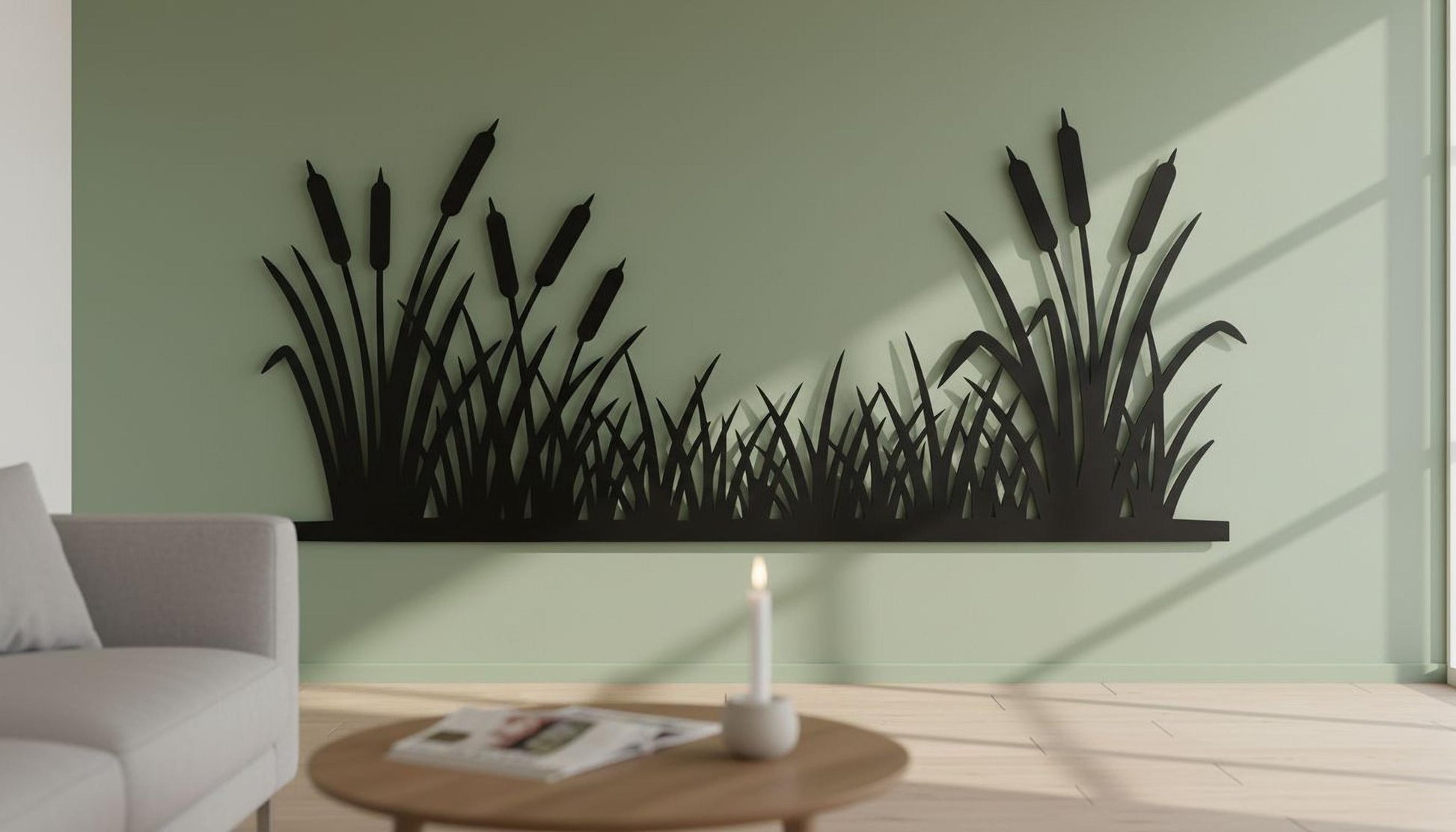 a living room with a green wall that has a large black silhouette of reeds or grasses. In front of the wall, there is a wooden coffee table with a lit candle on it. A couch is placed against the wall, and a magazine is visible on the coffee table.