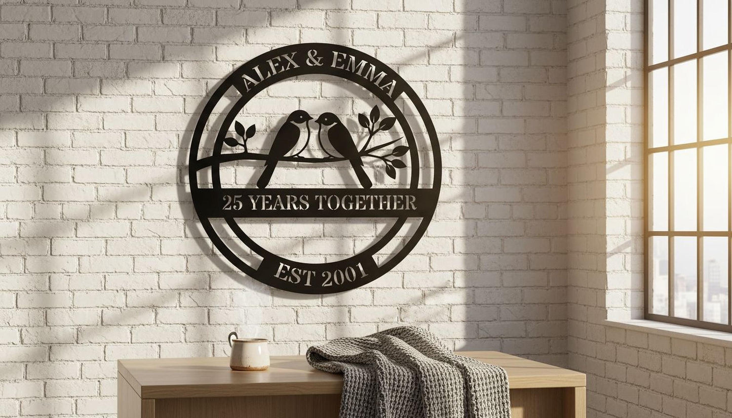 a decorative metal plaque with the text "Alex & Emma" and "25 YEARS TOGETHER EST 2001" on it, mounted on a white brick wall. Below the plaque, there is a wooden table with a cup and a blanket on it.