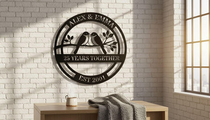 a decorative metal plaque with the text "Alex & Emma" and "25 YEARS TOGETHER EST 2001" on it, mounted on a white brick wall. Below the plaque, there is a wooden table with a cup and a blanket on it.