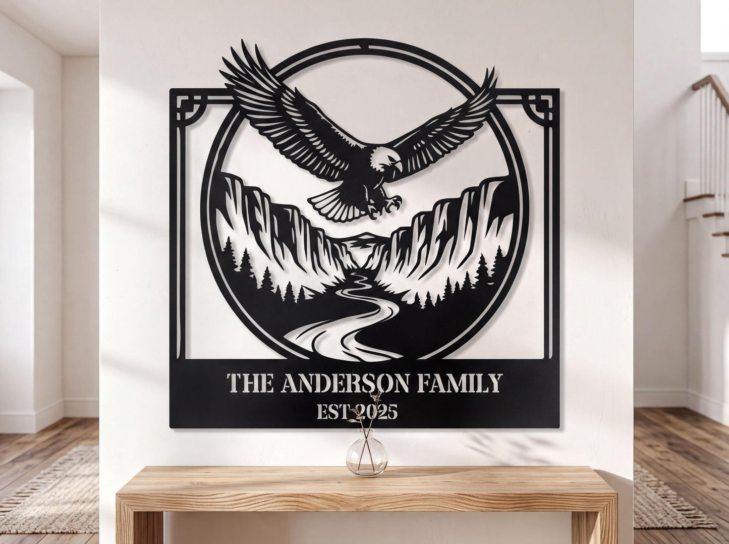 a large black and white metal wall art depicting an eagle in flight above a mountain landscape, with a river below. The text "THE ANDERSON FAMILY EST.2025" is displayed below the artwork.