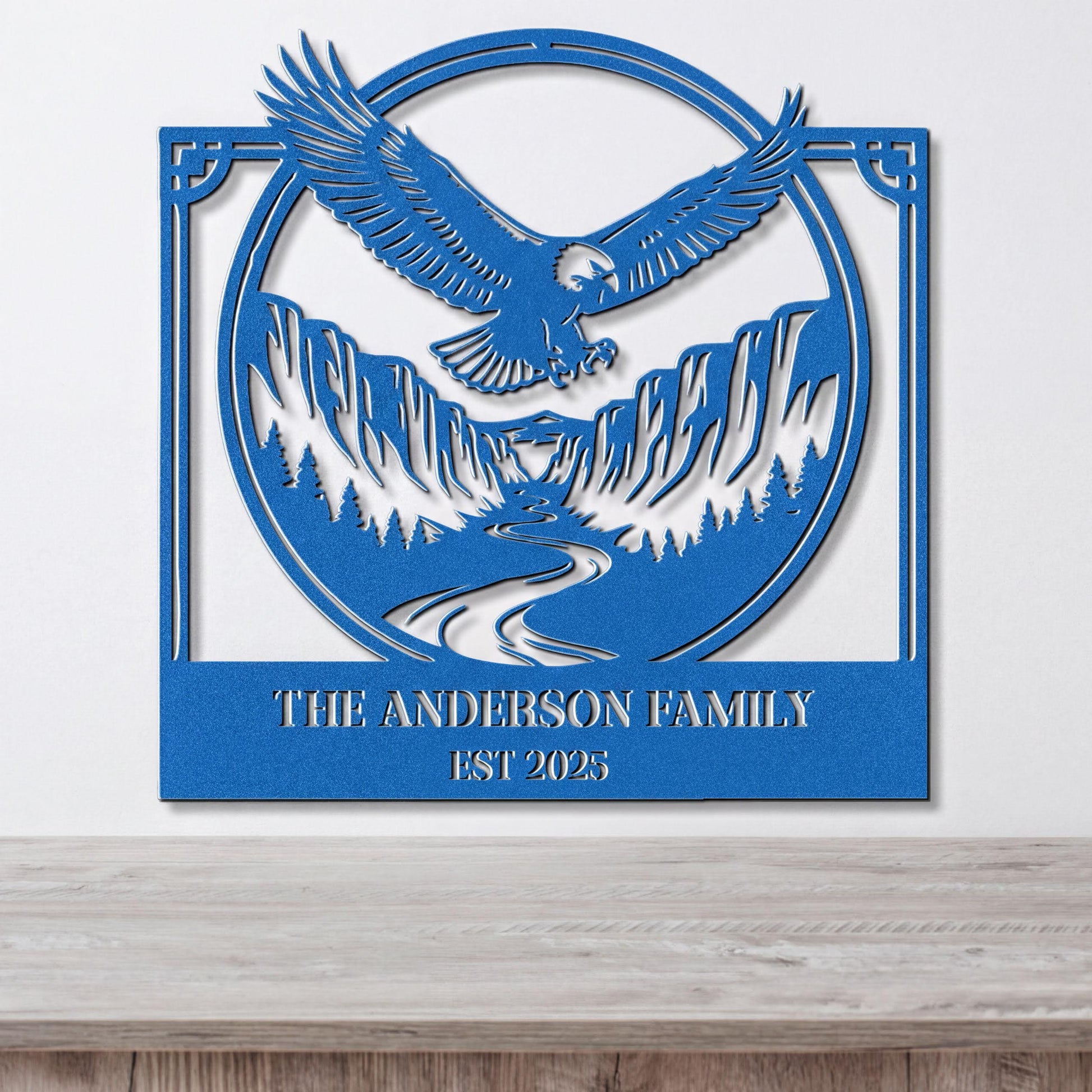 A blue metal wall art piece depicting an eagle in flight above a mountain landscape, with the text "THE ANDERSON FAMILY EST 2025" below the image.
