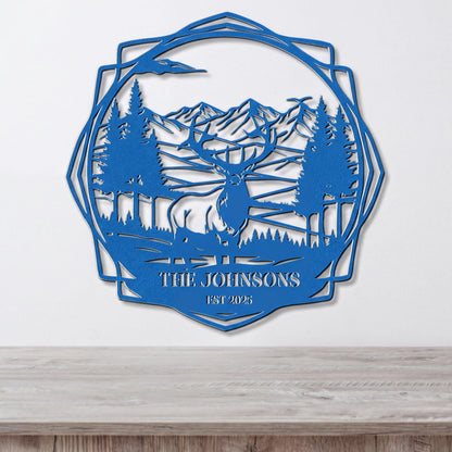 A blue metal wall hanging depicting a deer in a forest landscape with mountains in the background.