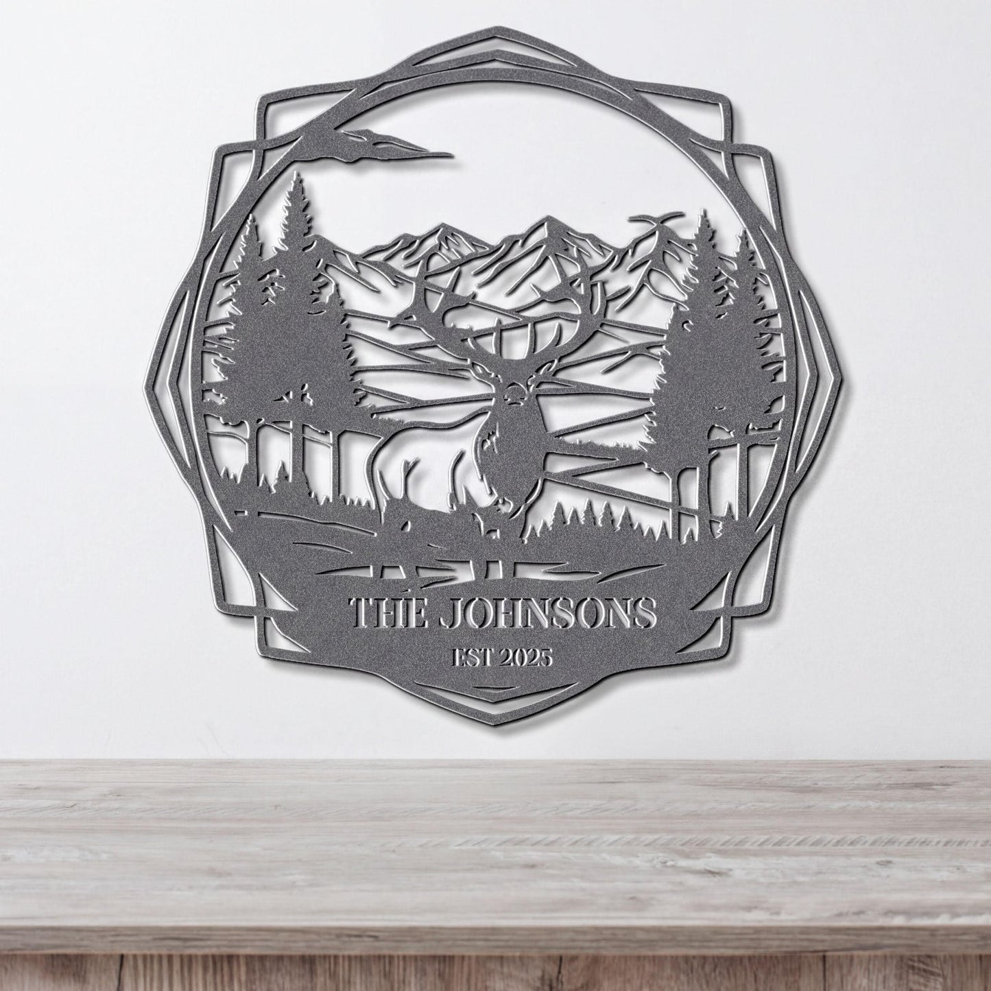 A metal wall art piece depicting a deer in a forest setting with mountains in the background.