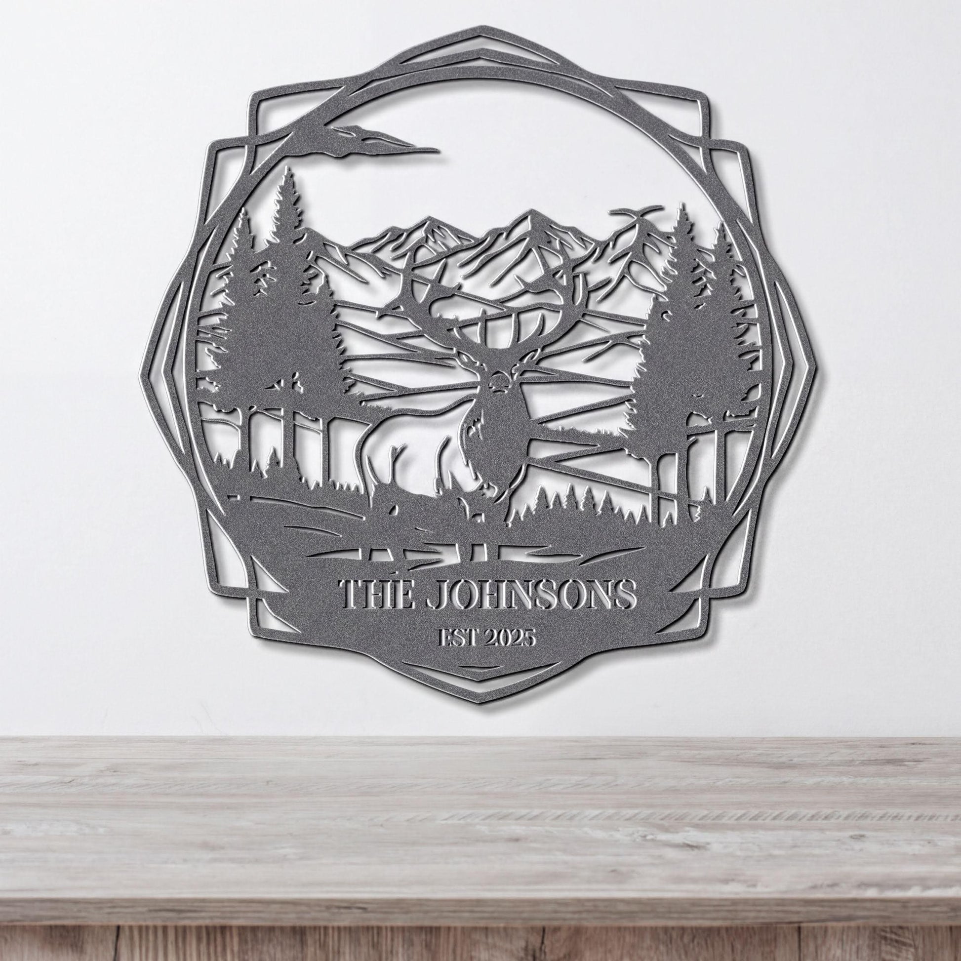 A metal wall art piece depicting a deer in a forest setting with mountains in the background.