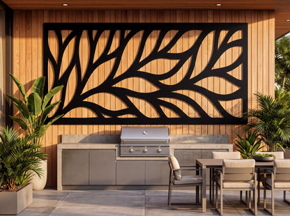 a modern outdoor kitchen with a large black leaf-shaped wall art piece above the grill, surrounded by potted plants and a dining table with chairs.