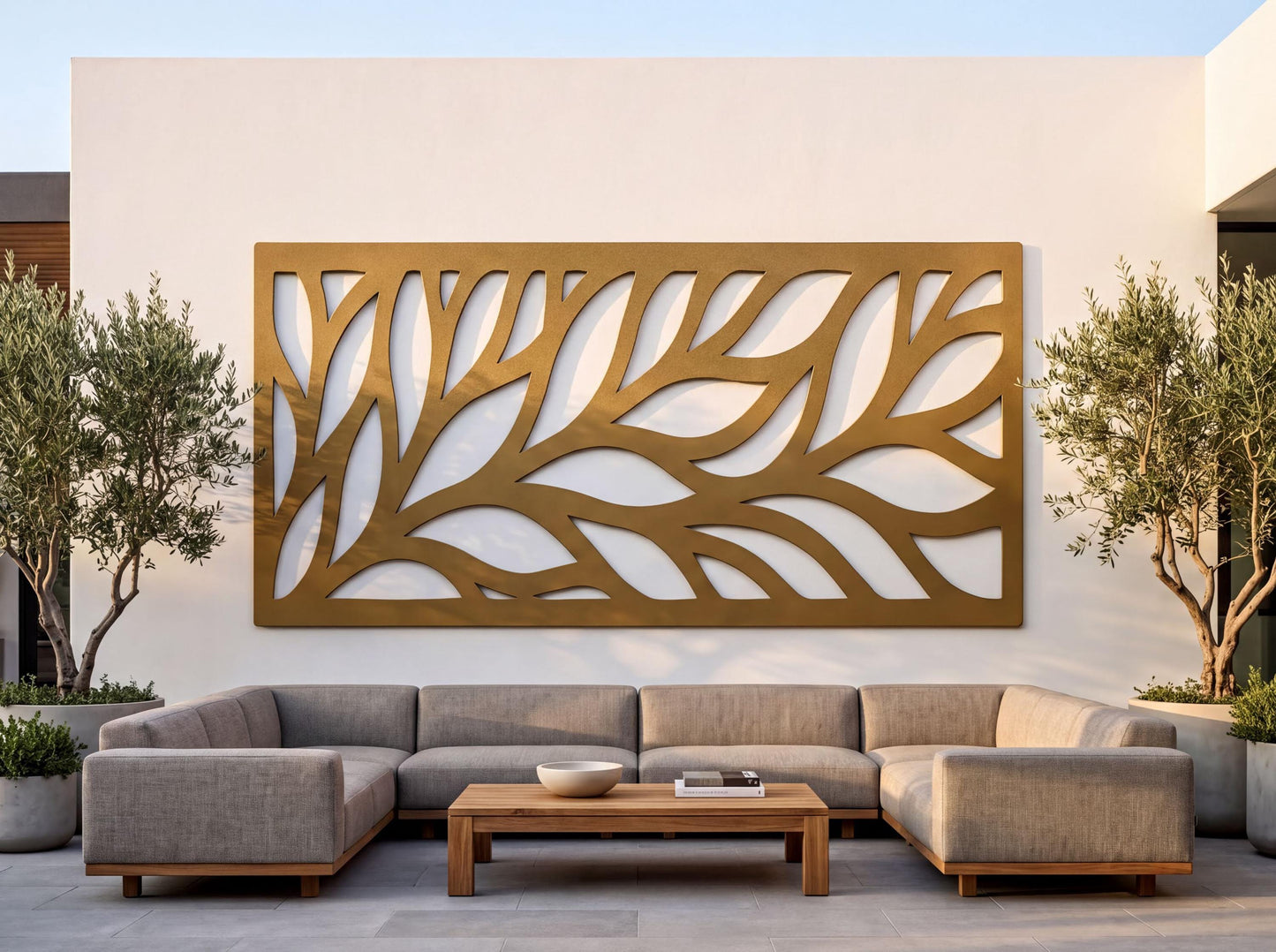 a modern outdoor living space with a large, abstract wall art piece in gold and white colors. The wall art is mounted on a white wall, and it is positioned between two potted plants. In front of the wall art, there is a comfortable seating arrangement consisting of a gray sofa and a wooden coffee table.
