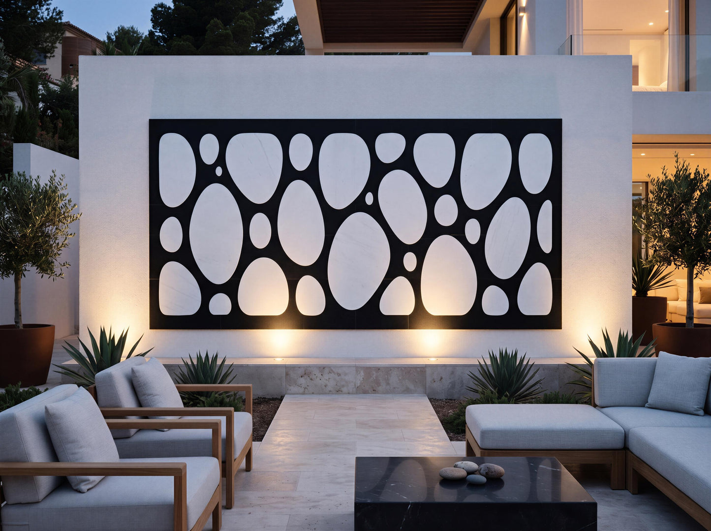 a modern outdoor living space with a large black and white abstract design on the wall behind a seating area. The seating area consists of two couches and two chairs, arranged around a coffee table. The space is illuminated by warm lighting, creating a cozy and inviting atmosphere.