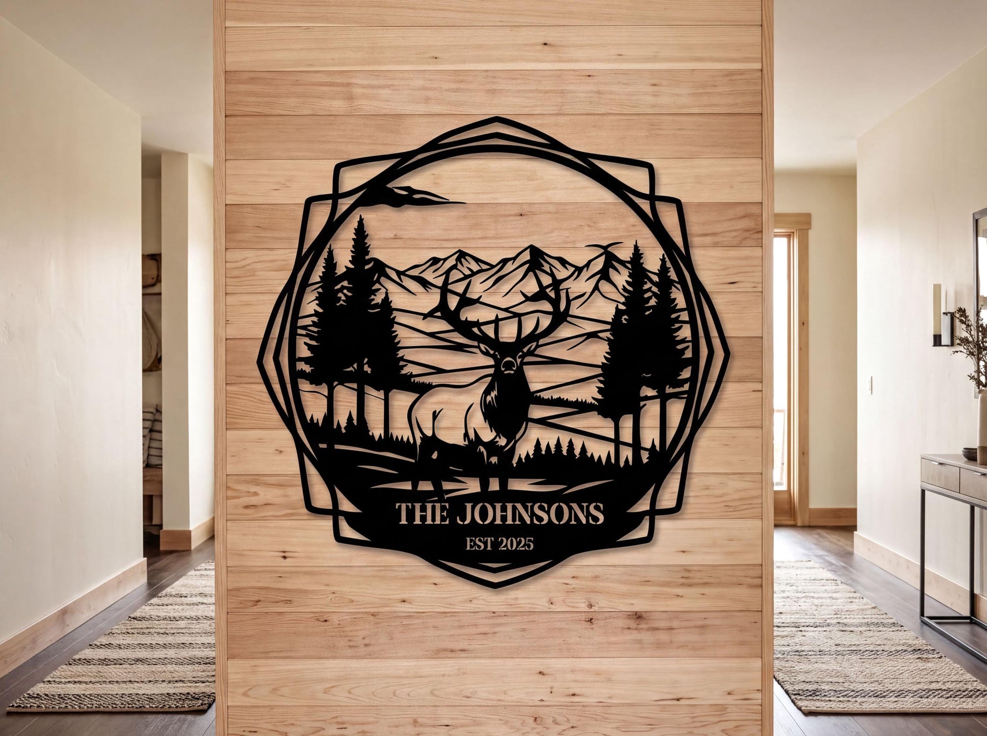 a wooden wall with a decorative metal design depicting a deer in a forest setting, surrounded by mountains. The text "THE JOHNSONS EST. 2005" is displayed below the deer, indicating the name and year of the family.
