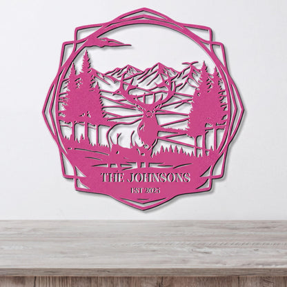 A pink metal wall hanging depicting a deer in a forest landscape with mountains in the background.