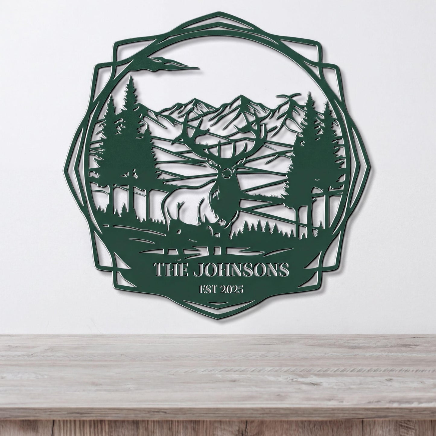 A metal wall art piece depicting a deer in a forest setting with mountains in the background.
