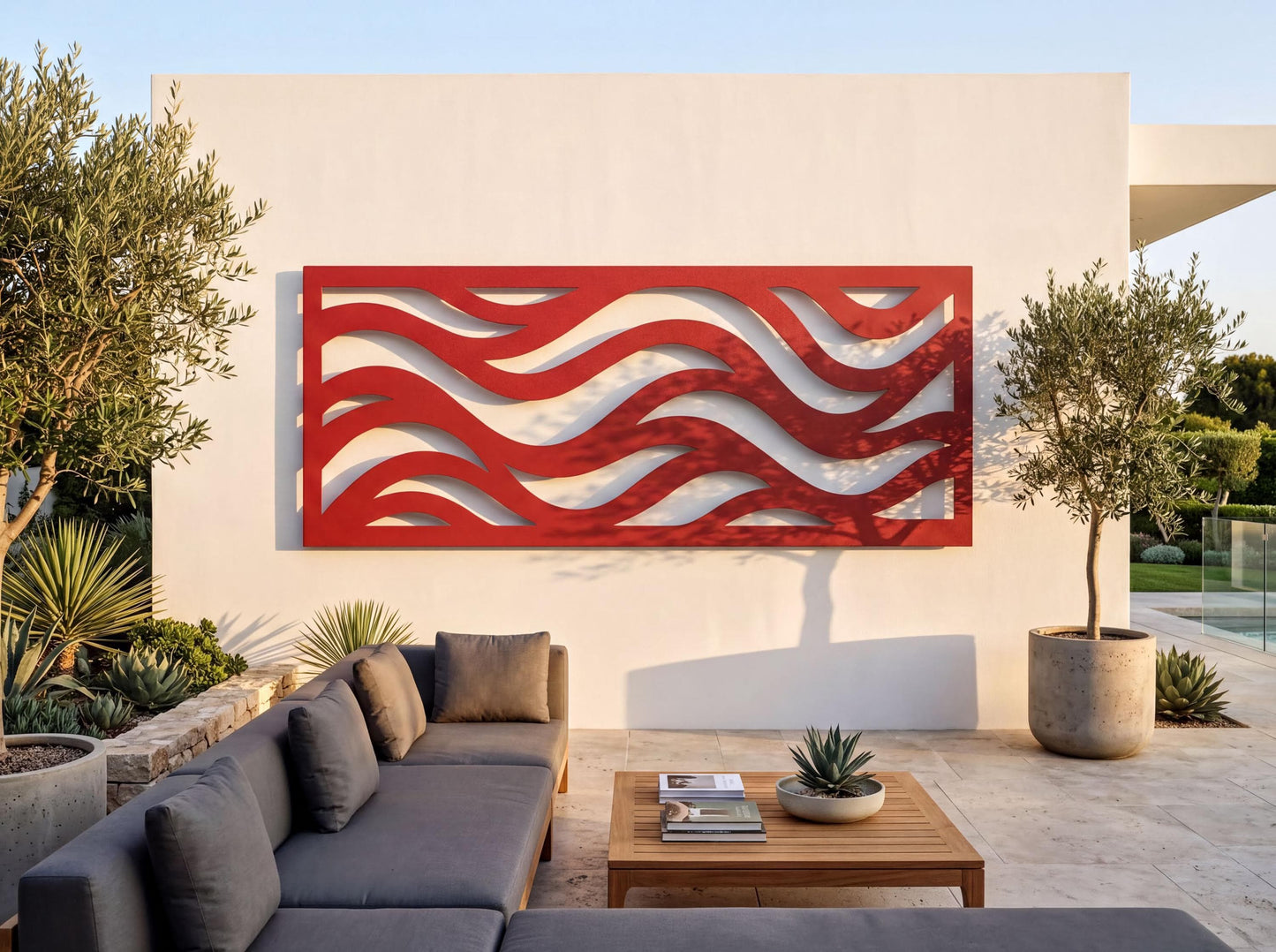 a modern outdoor living space with a gray sofa, a wooden coffee table, and a large red abstract wall art piece. The space is surrounded by lush greenery, including potted plants and trees, creating a serene and inviting atmosphere.