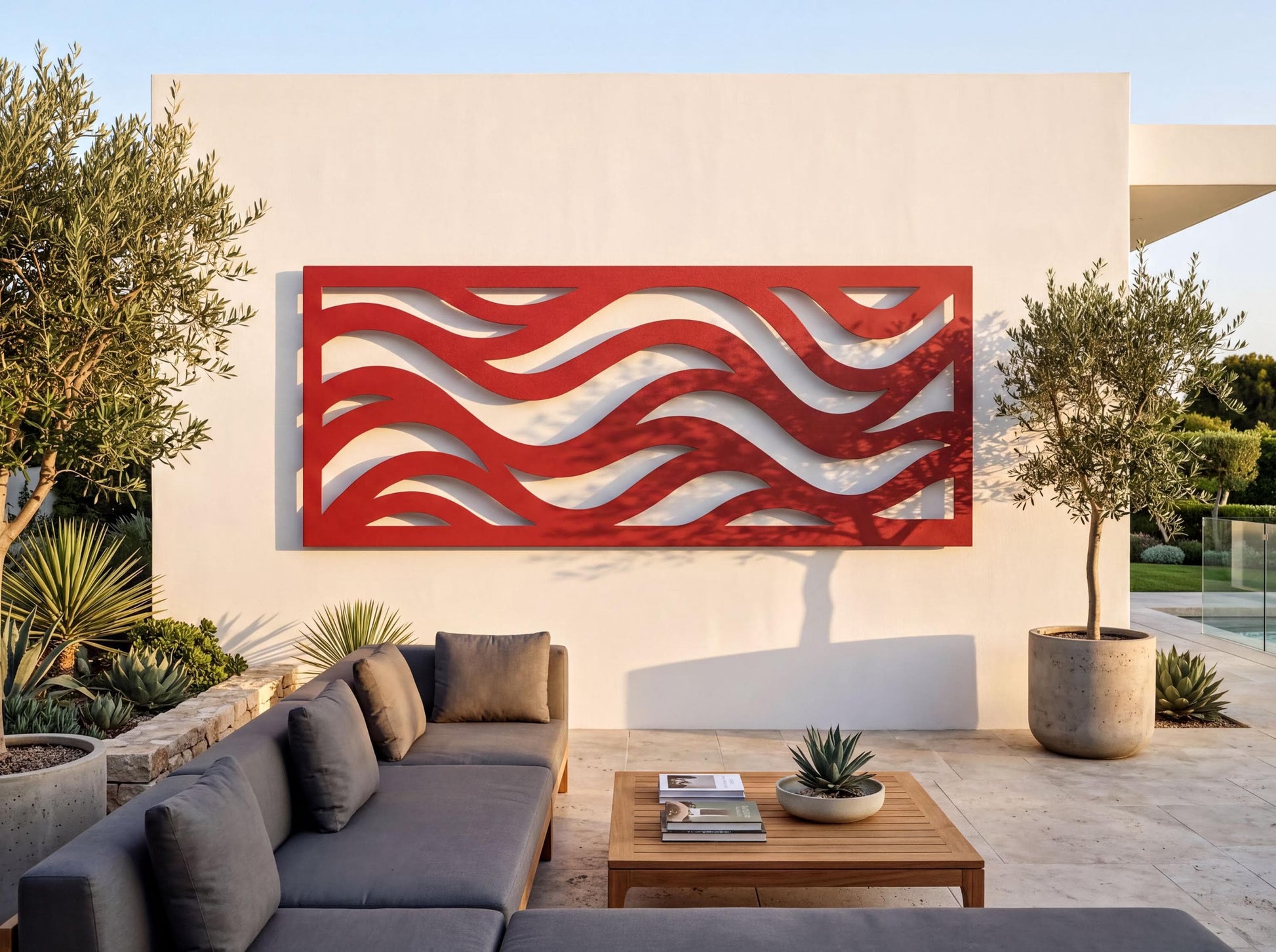 a modern outdoor living space with a gray sofa, a wooden coffee table, and a large red abstract wall art piece. The space is surrounded by lush greenery, including potted plants and trees, creating a serene and inviting atmosphere.