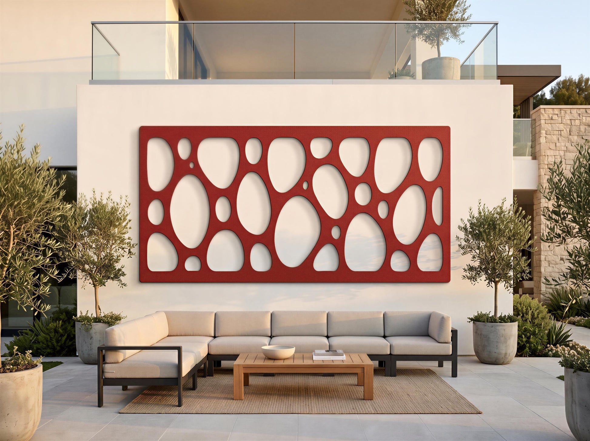 a modern outdoor living space with a large red circular wall art piece, a gray sectional sofa, and a wooden coffee table. The space is surrounded by potted plants and a glass railing, creating a comfortable and inviting atmosphere.