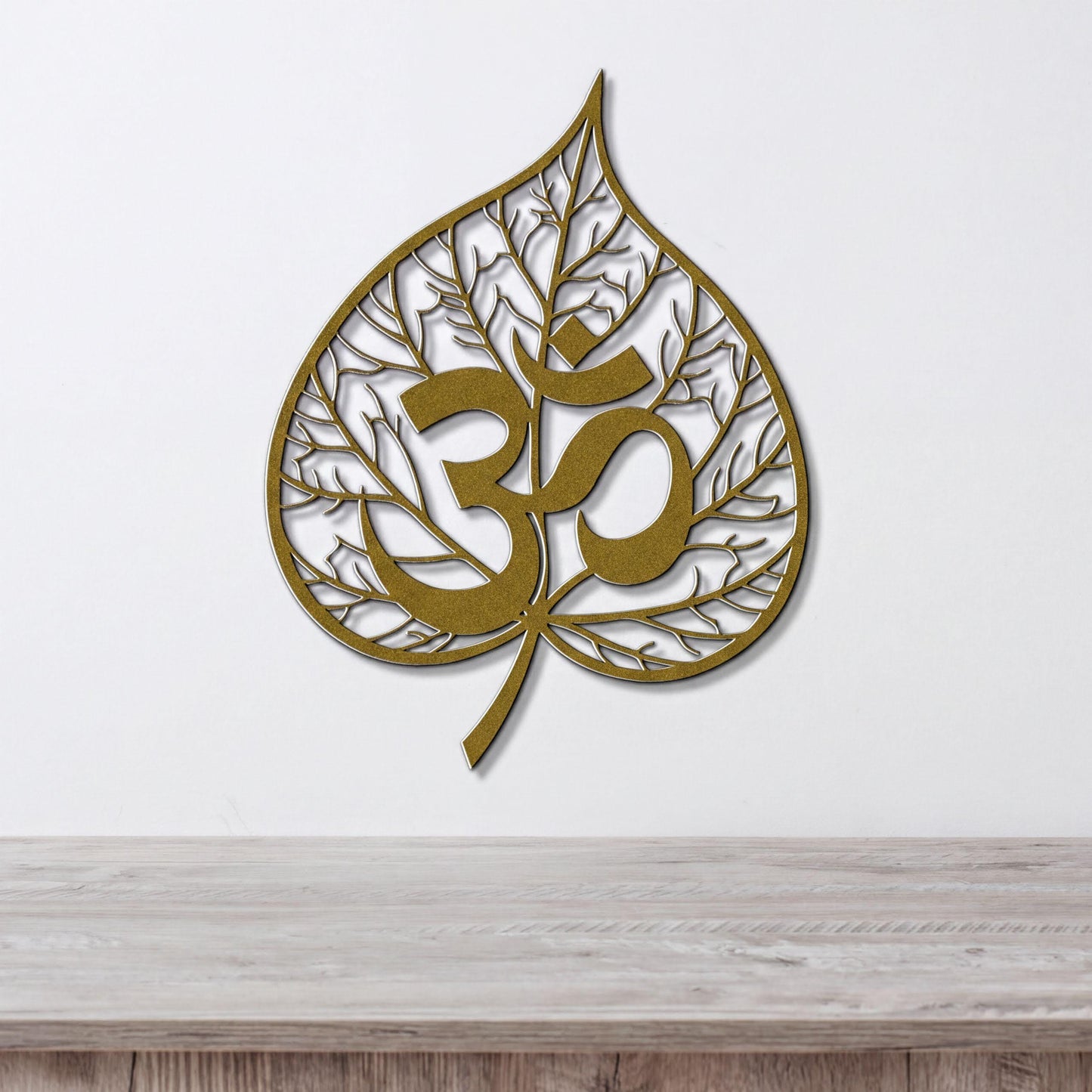 a gold leaf-shaped wall art with the Om symbol inside it, hanging on a white wall above a wooden table.
