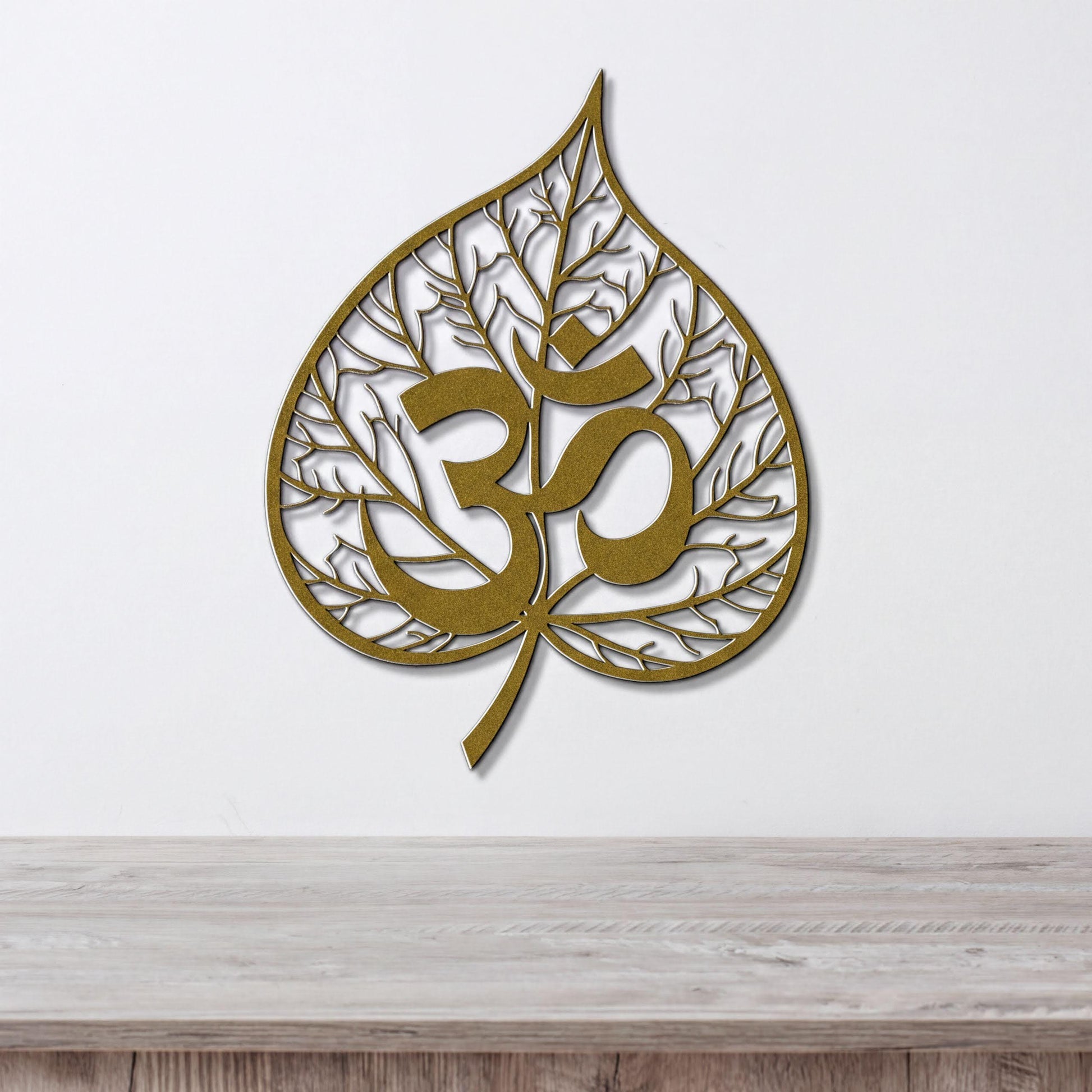 a gold leaf-shaped wall art with the Om symbol inside it, hanging on a white wall above a wooden table.